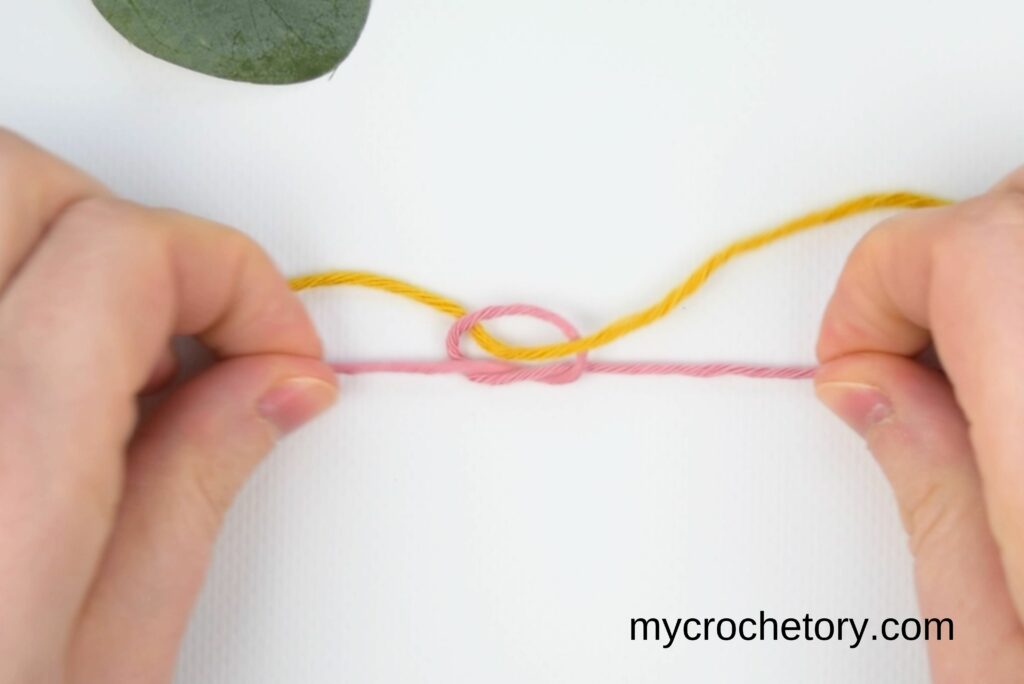Tightening the magic knot for joining yarn to create a secure join.