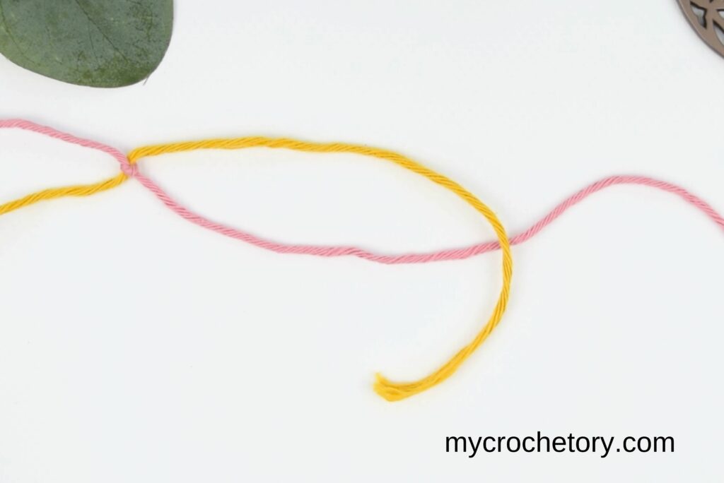 Bringing the yellow yarn over the pink yarn to tie the magic knot for joining yarn.