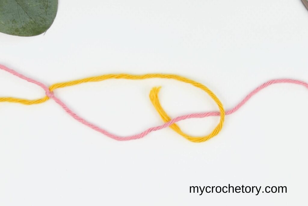 Yellow yarn pulled under the pink yarn, forming a knot in the magic knot for joining yarn.