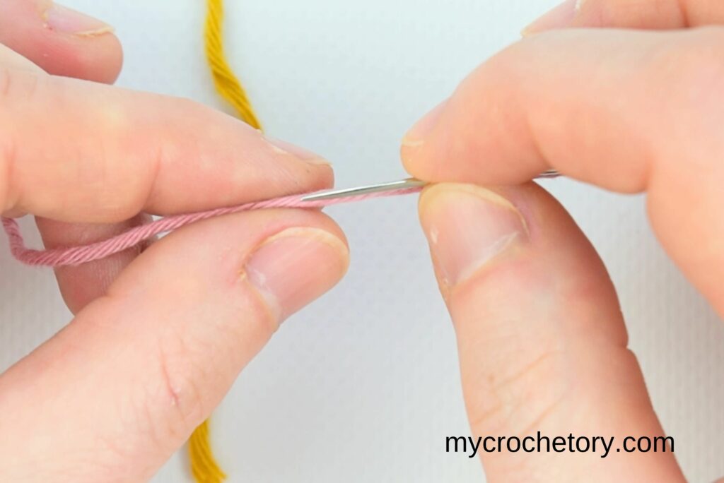 A needle being inserted into pink yarn to create a secure connection for how to join yarn ends.