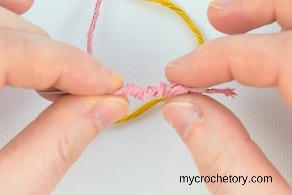 Pink yarn wrapped around a needle to form a loop, showing how to join yarn ends.