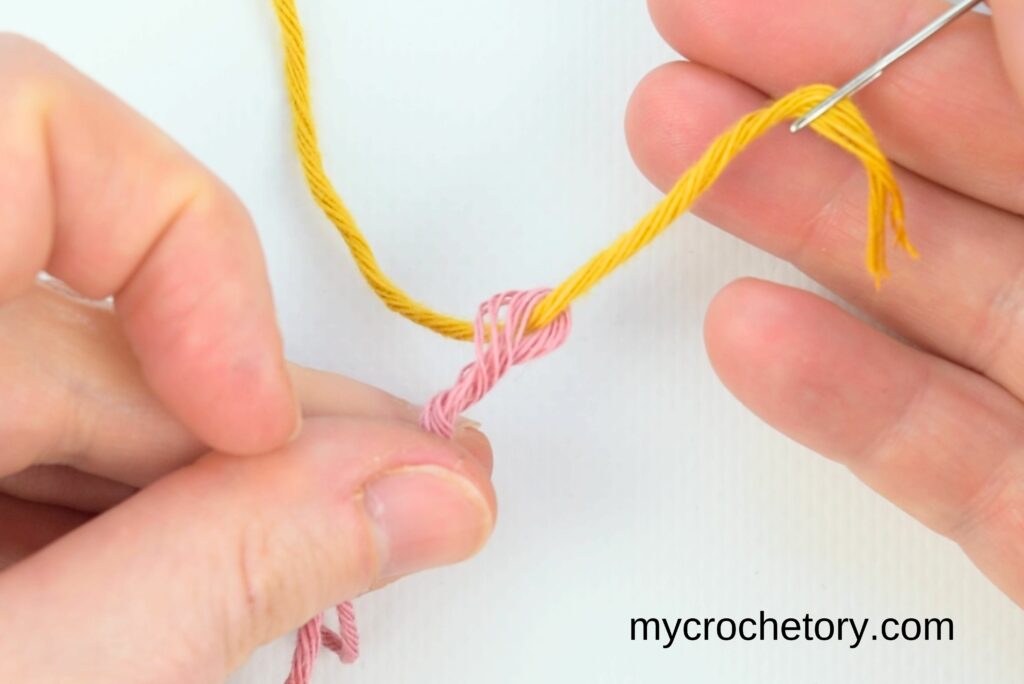Weaving yellow yarn with a needle to finish how to do a Russian join.