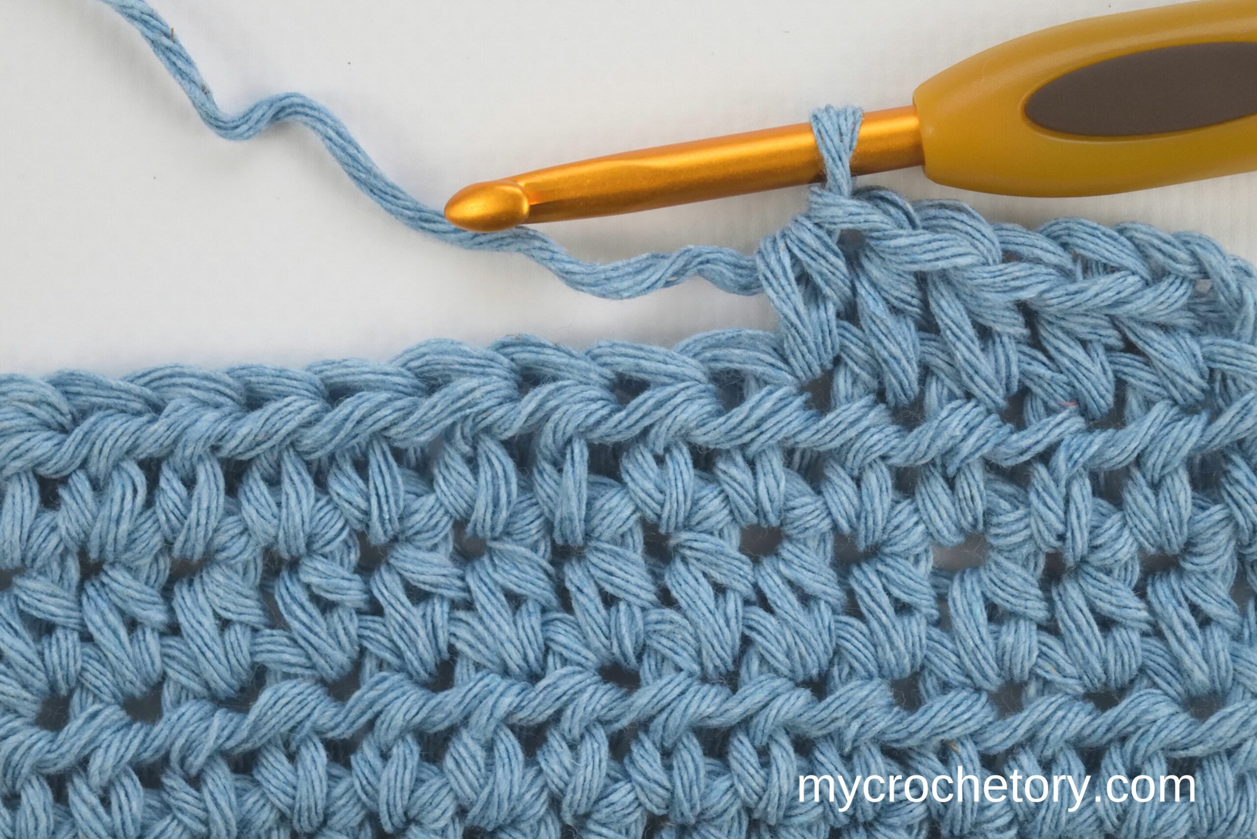 Blue half double crochet swatch with a crochet hook in the last stitch