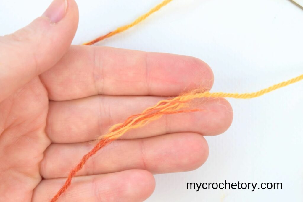 Orange and yellow yarn strands overlapped to begin how to join yarn ends.
