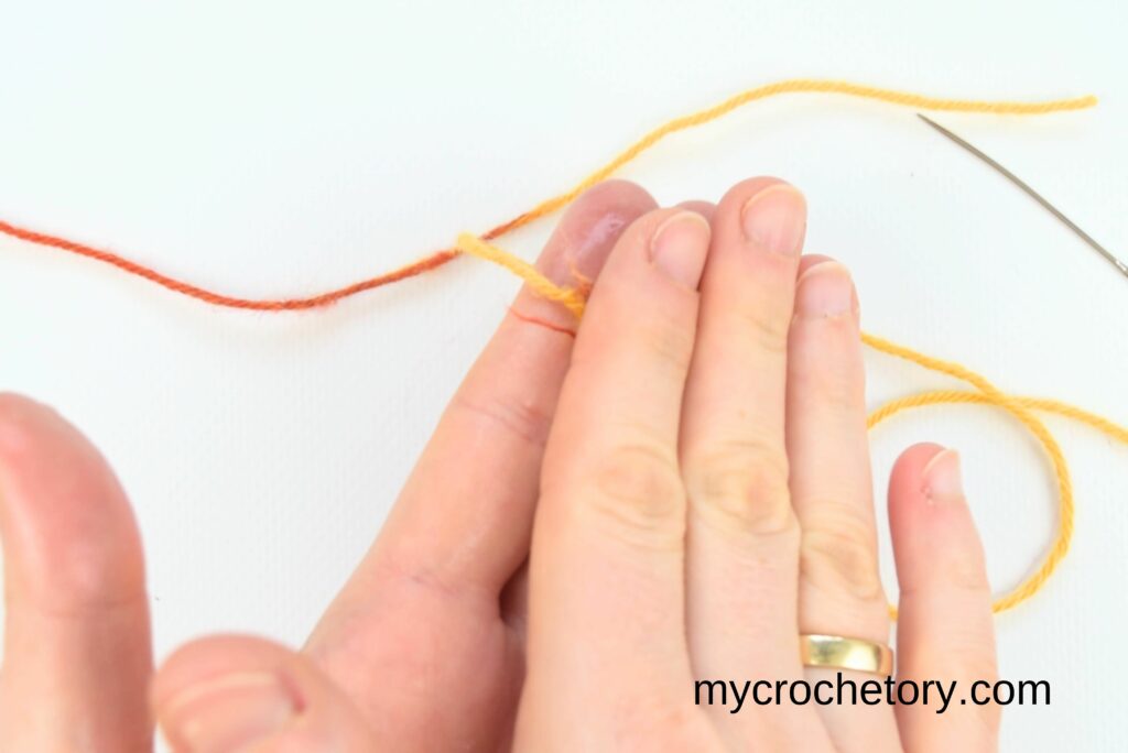 Hands rubbing wet yarn ends together to securely connect them, demonstrating how to join yarn ends.