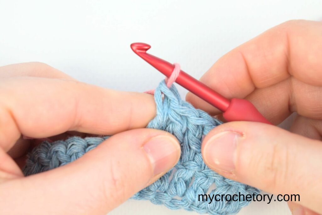 Completing the stitch with pink yarn to show how to join yarn ends.