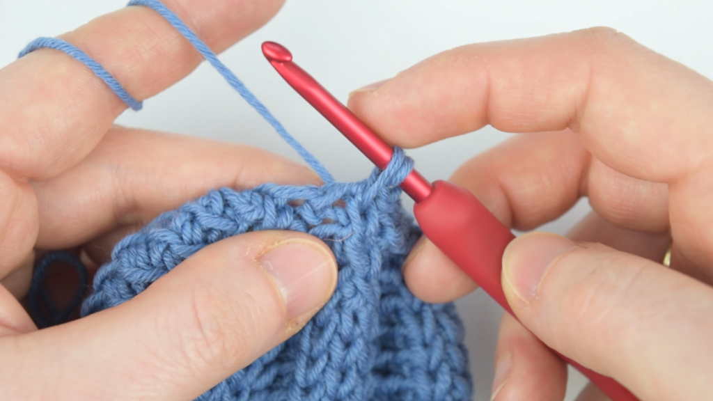 Close-up of blue yarn and crochet hook in action for a chunky crochet hat project.