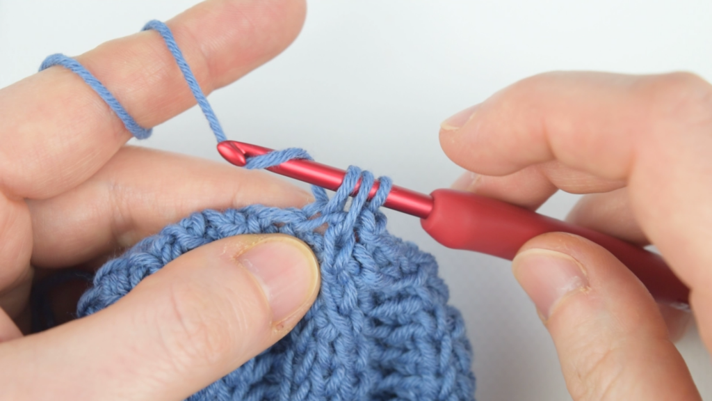 Hands working on decrease stitches for a chunky crochet hat with blue yarn.