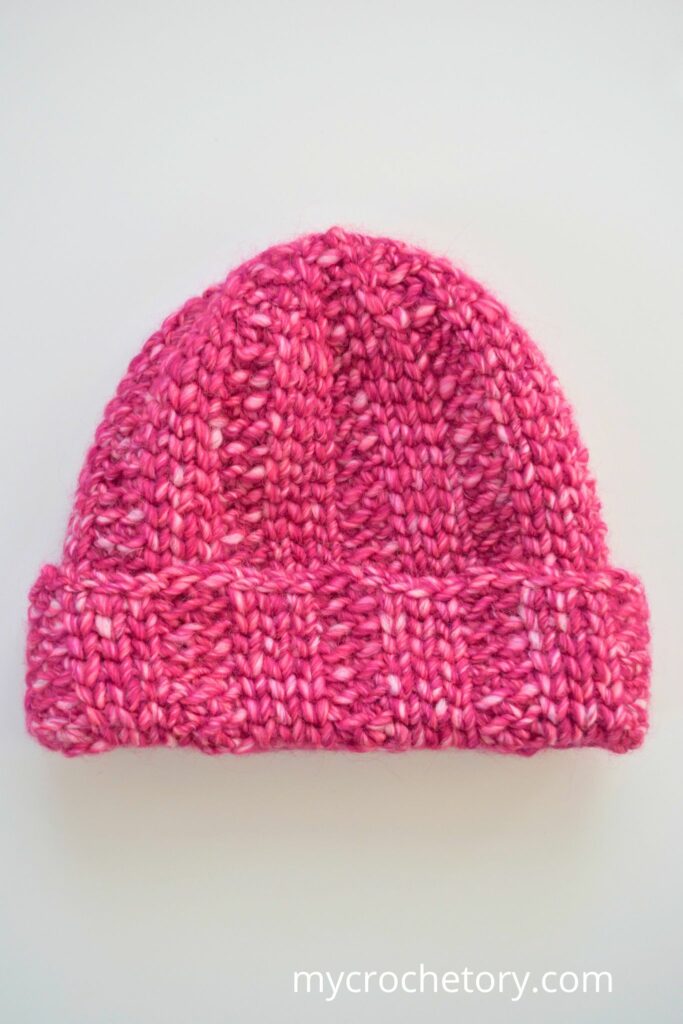 Pink chunky crochet hat with folded brim on a white background.