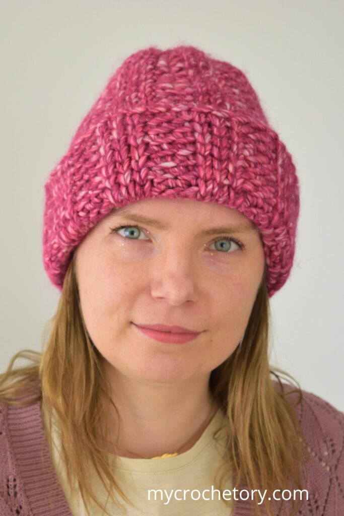 Front view of a pink chunky crochet hat modeled by a woman.