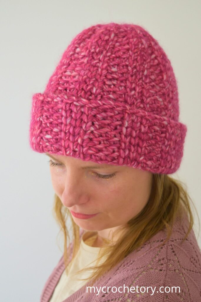 Woman modeling a chunky crochet hat with knit-like texture in pink.