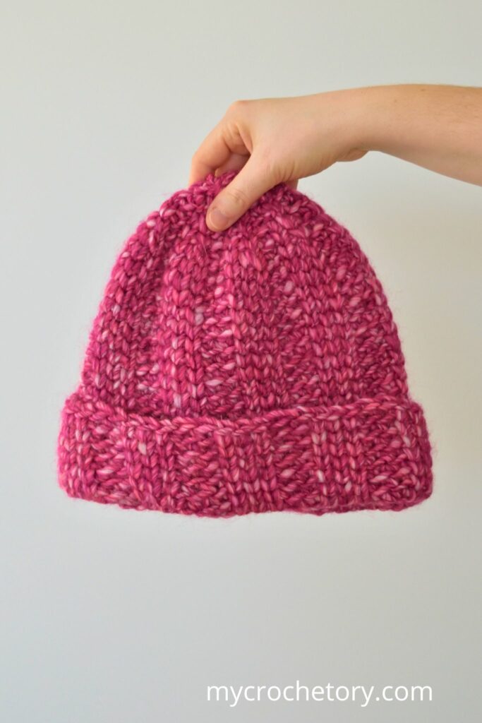 Hand holding a pink chunky crochet hat with a ribbed brim.