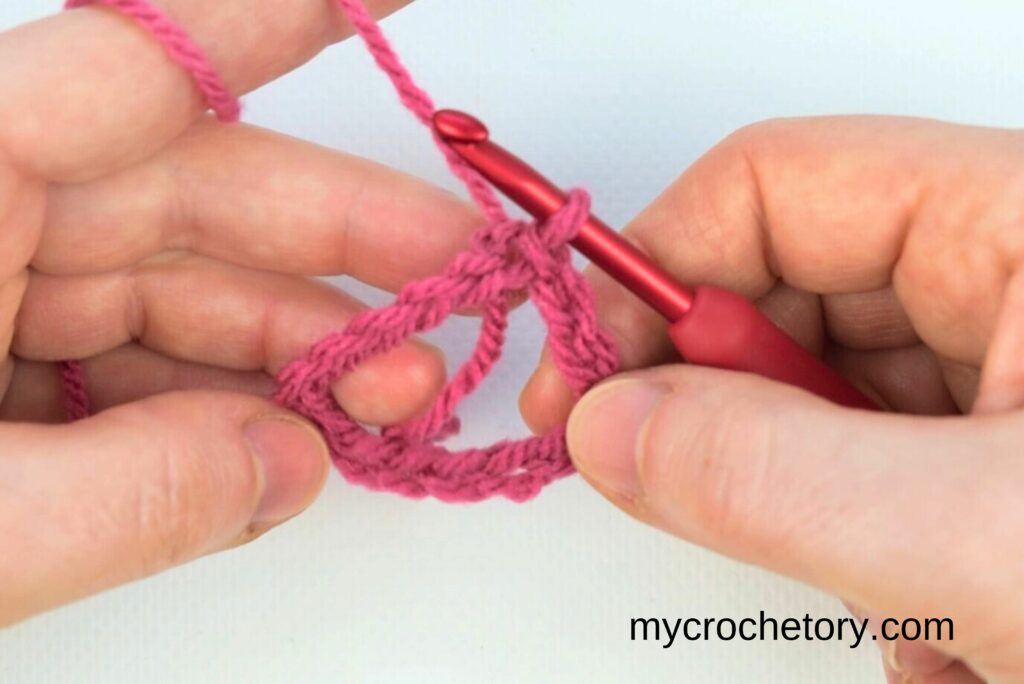 Hands holding a crochet hook and pink yarn, forming a foundation chain for the crochet waistcoat stitch tutorial.