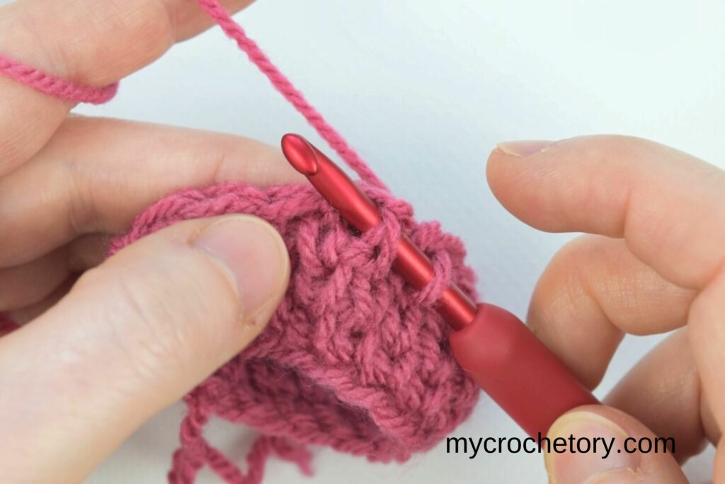 Bringing the hook from back to front between two decreasing stitches in the crochet waistcoat stitch for a seamless finish.