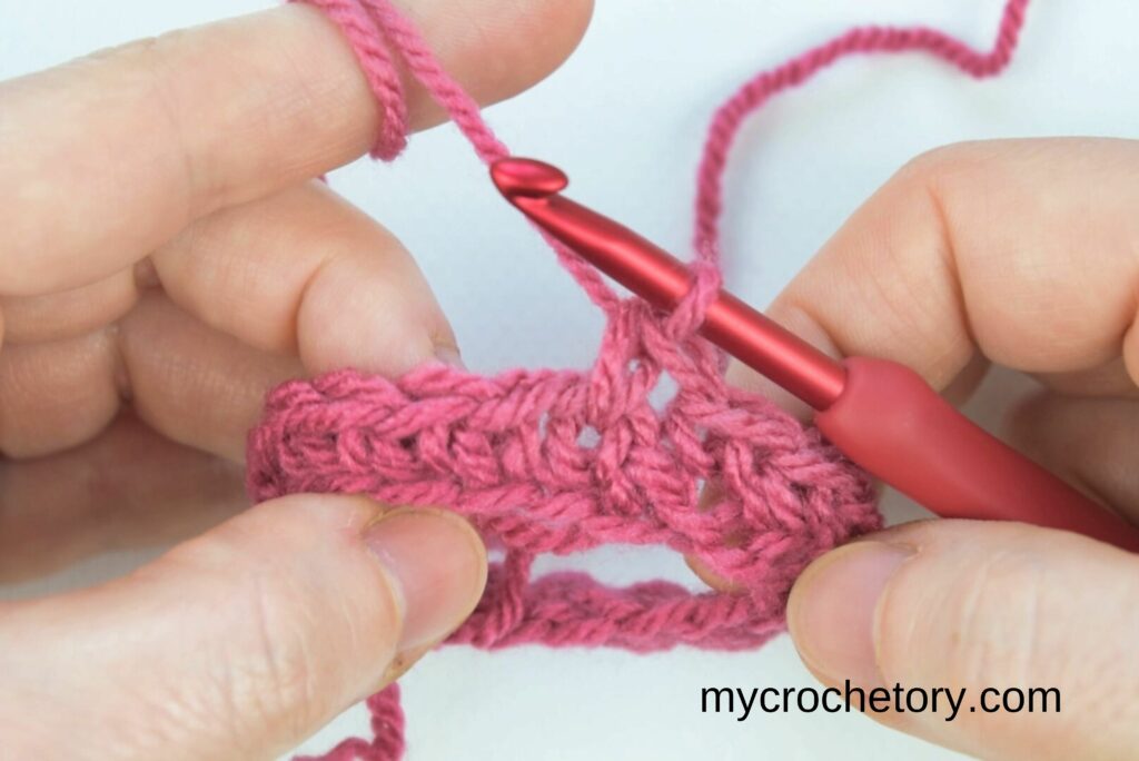 Hands showing the proper hook placement for the crochet waistcoat stitch in a round.