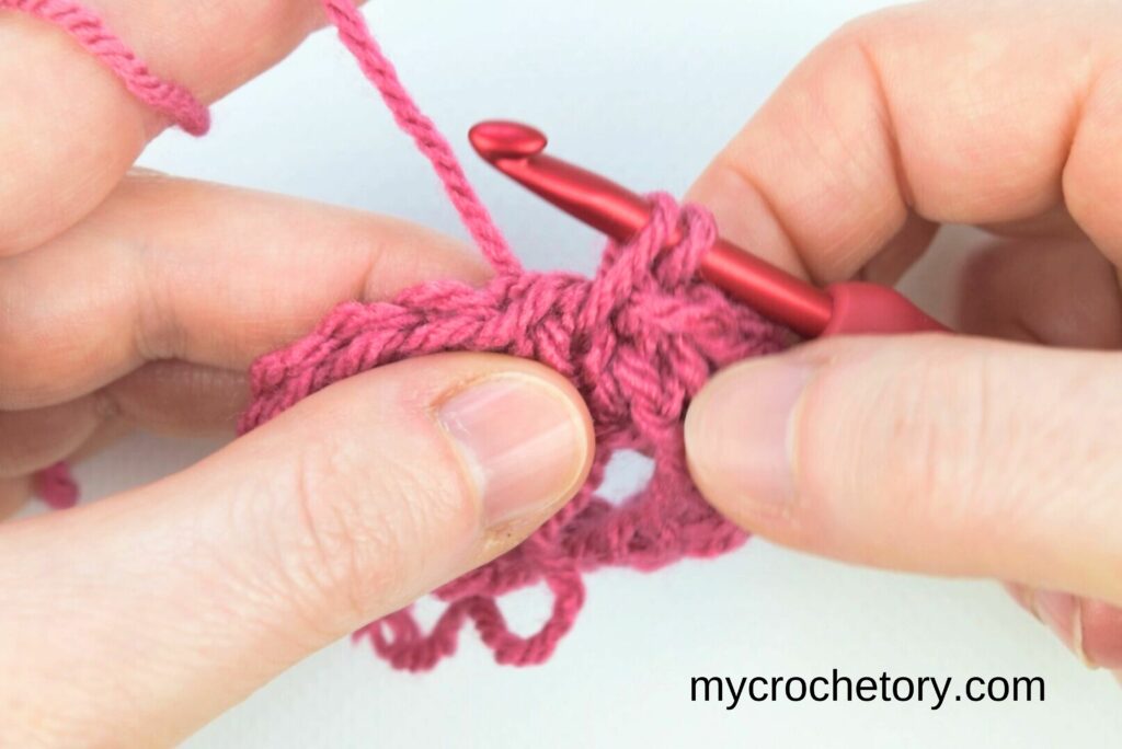 Working the crochet waistcoat stitch by pulling up a loop through the vertical bars of the stitch.
