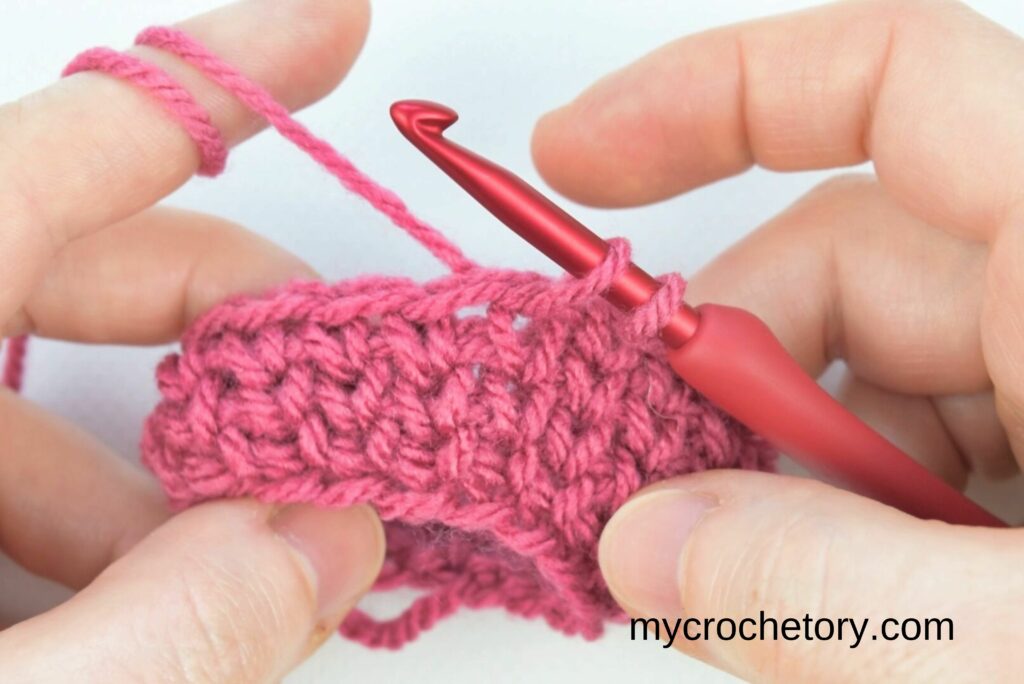 Starting the first decrease method for the crochet waistcoat stitch by inserting the hook into the first stitch.