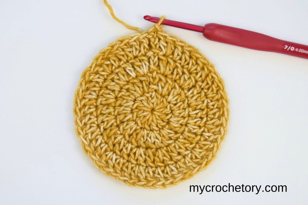 Close-up of how to crochet a circle with double crochet stitches and a red crochet hook.