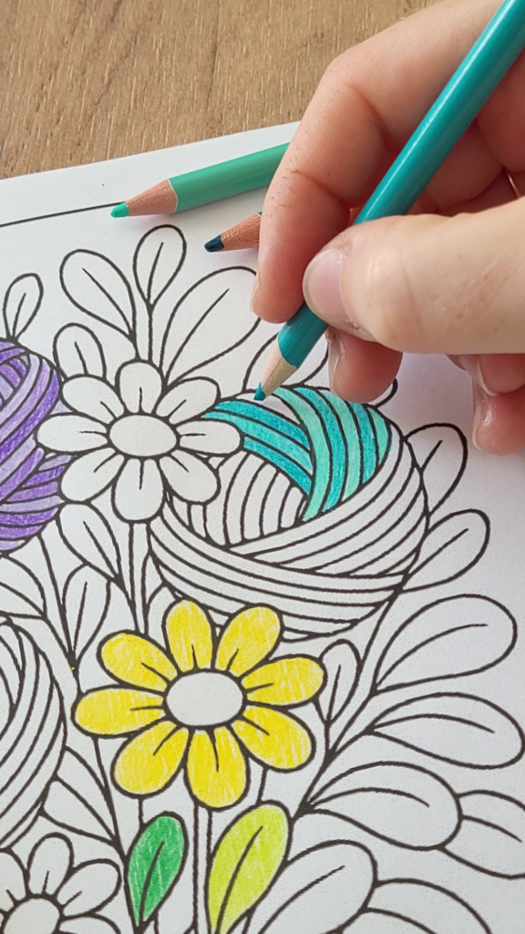 Hand coloring a detailed yarn-and-flower page from a crochet coloring book with a turquoise pencil.