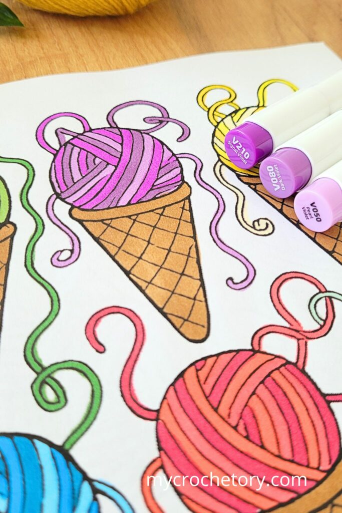 Colorful yarn balls in ice-cream cones on a crochet coloring book page with markers at the edge.