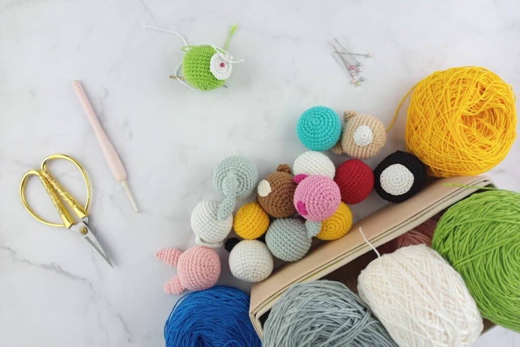 Colorful pile of amigurumi heads and yarn balls on a white table — behind-the-scenes of easy crochet amigurumi assembly tricks.