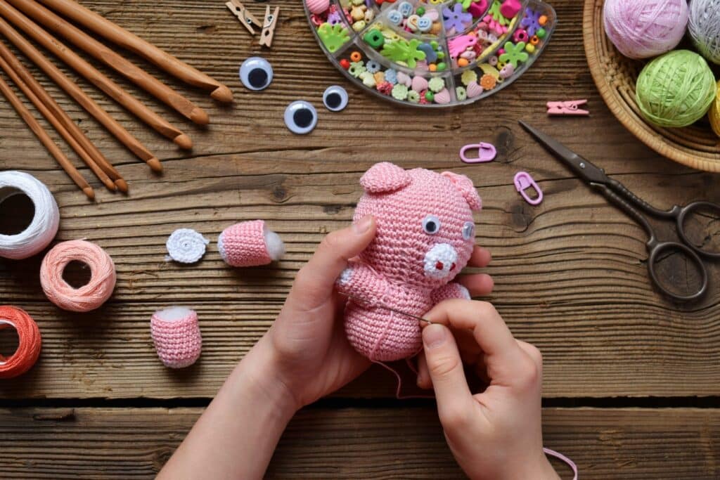 Hands sewing a pink crochet pig with visible stuffing and limbs — realistic process using easy crochet amigurumi tricks.
