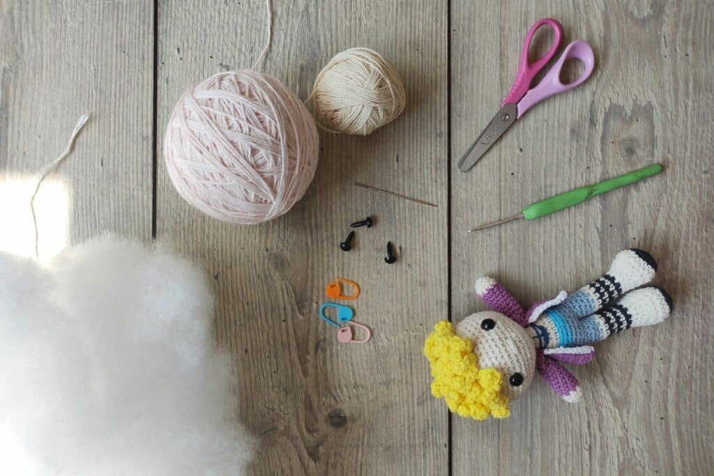 Yarn, stuffing, and an unfinished doll with curly yellow hair — setup showing tools used in easy crochet amigurumi hacks.