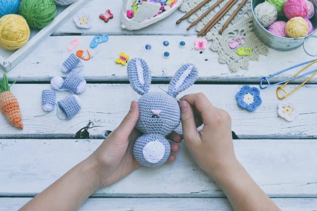 Close-up of a blue amigurumi bunny being assembled on a white background — clear view of easy crochet amigurumi tricks in progress.
