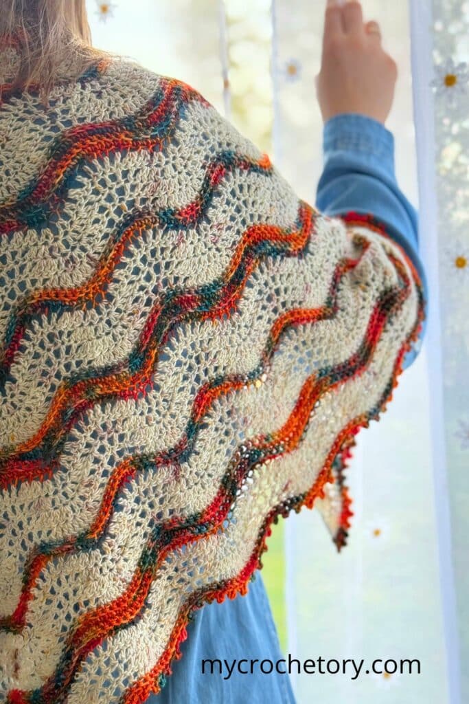 Close-up of the Norra boho shawl crochet pattern showing soft lace and wavy stripes in warm tones.