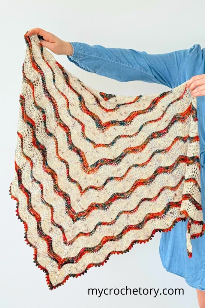 Full view of the Norra boho shawl crochet pattern held up to show its ripple design and texture.