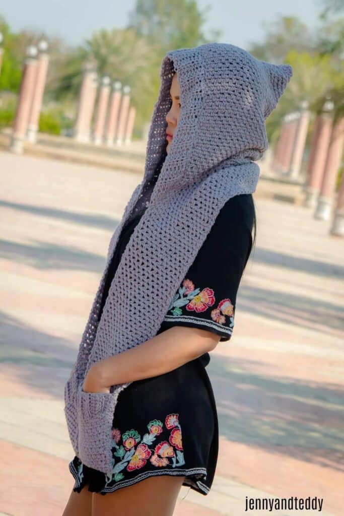 Woman wearing a light gray crochet hooded scarf with front pockets, handmade and lightweight for fall weather.