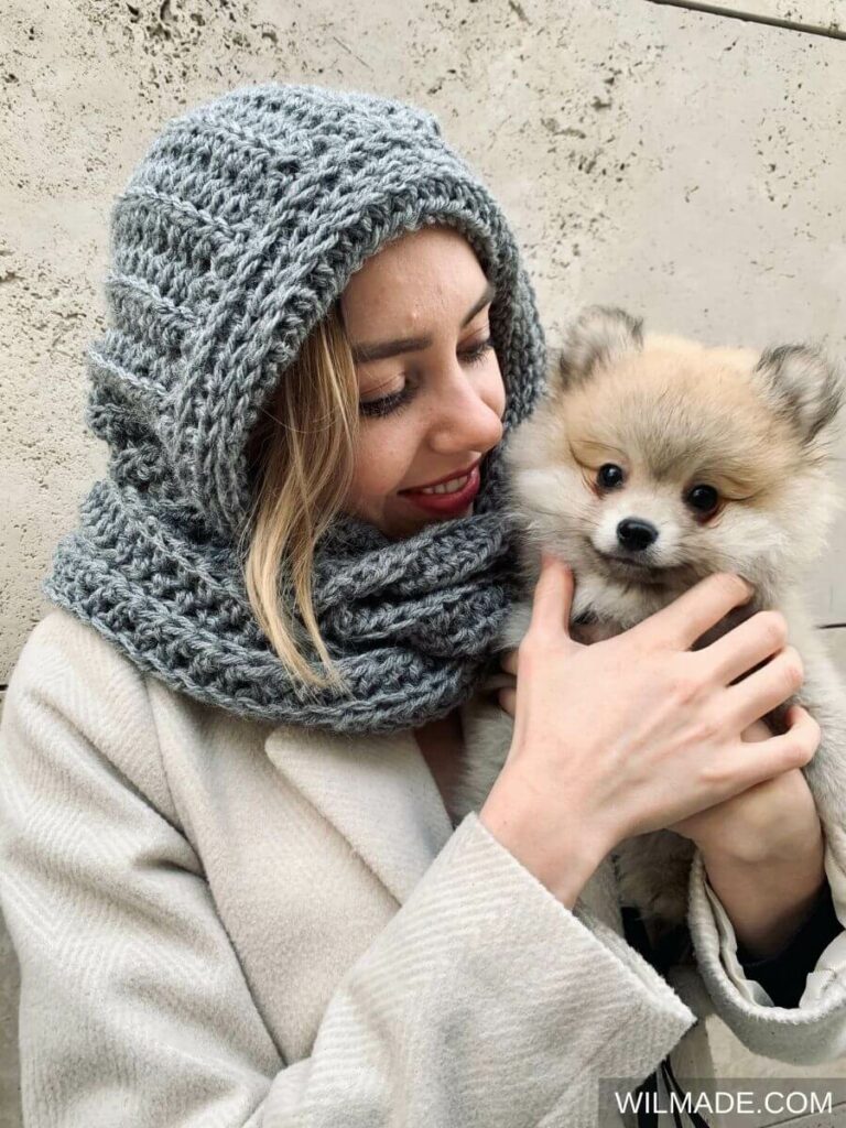 Woman in a gray coat wearing a chunky gray crochet hooded scarf, handmade for warmth and comfort.