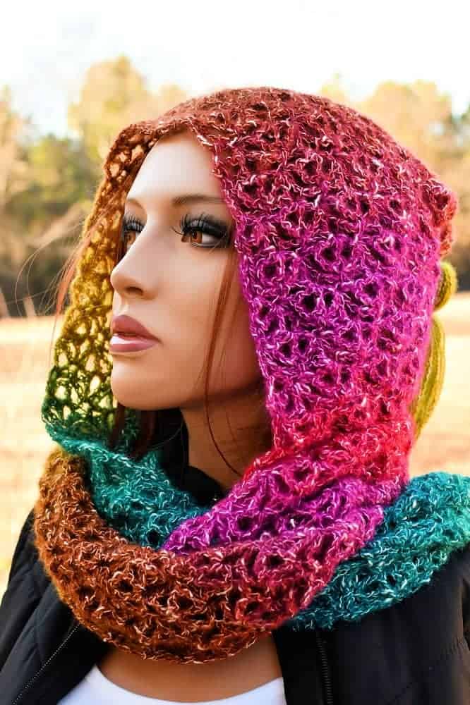 Woman wearing a colorful crochet hooded infinity scarf made with lace stitches and gradient yarn, a stylish and cozy handmade accessory.