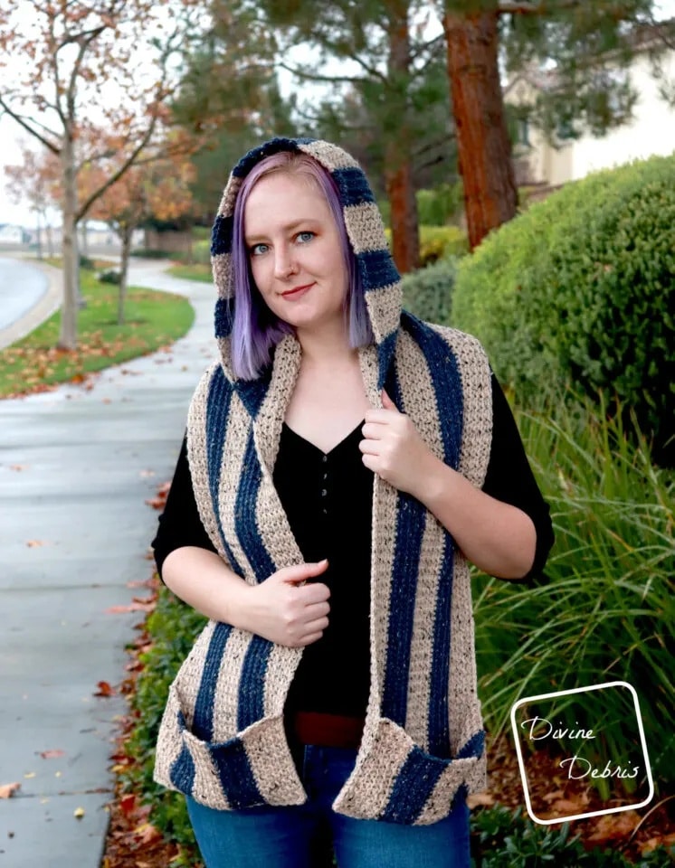 Woman wearing the Artemis crochet hooded scarf with blue and tan stripes, showing cozy pockets and relaxed fit.