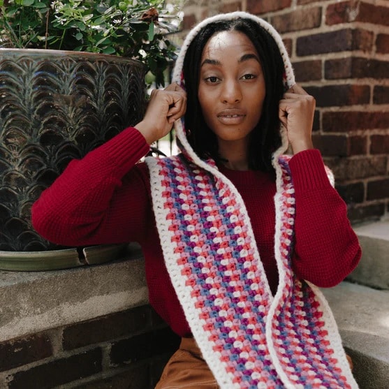 Woman adjusting a colorful crochet hooded scarf made with classic linen stitch pattern in red and pink tones.