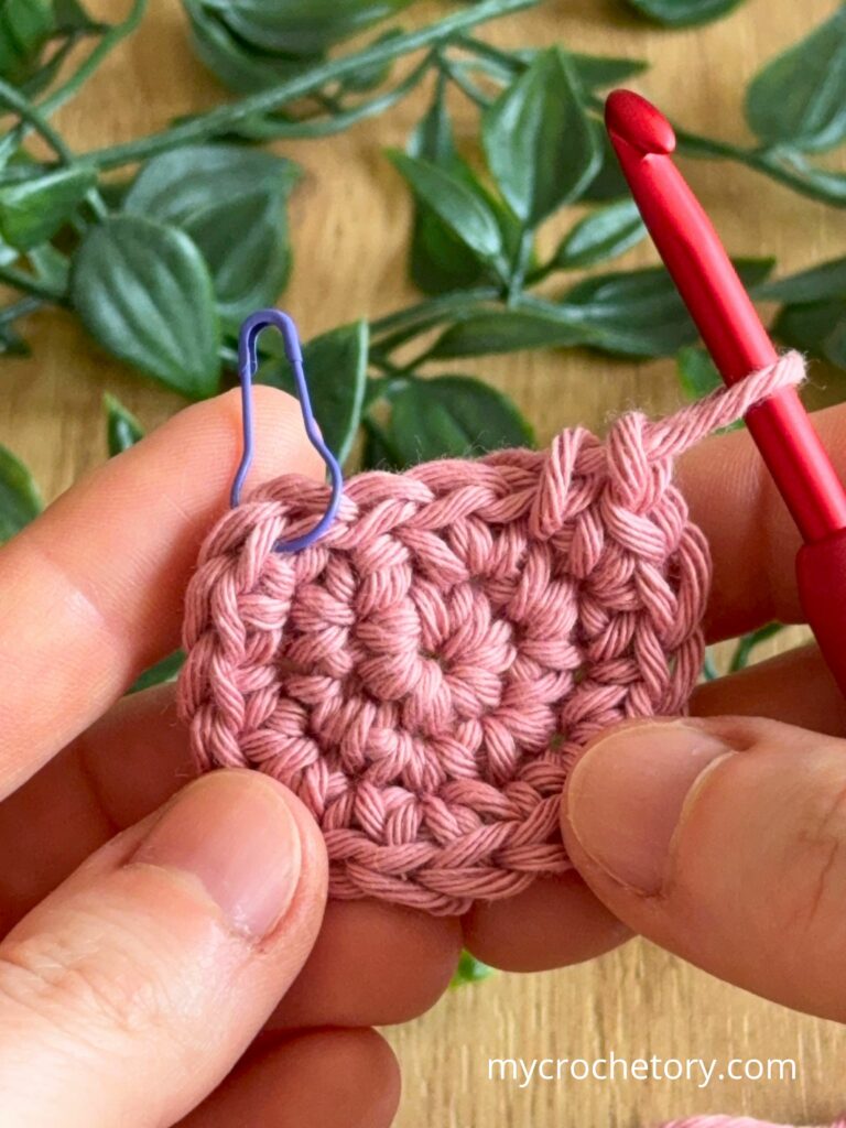 Crochet circle in progress with hook and stitch marker showing even stitches