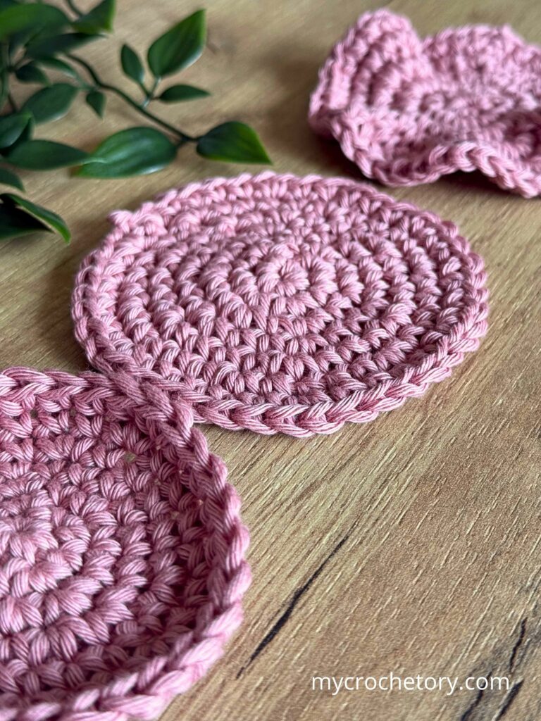 Flat crochet circles and a slightly curling crochet circle on wooden table