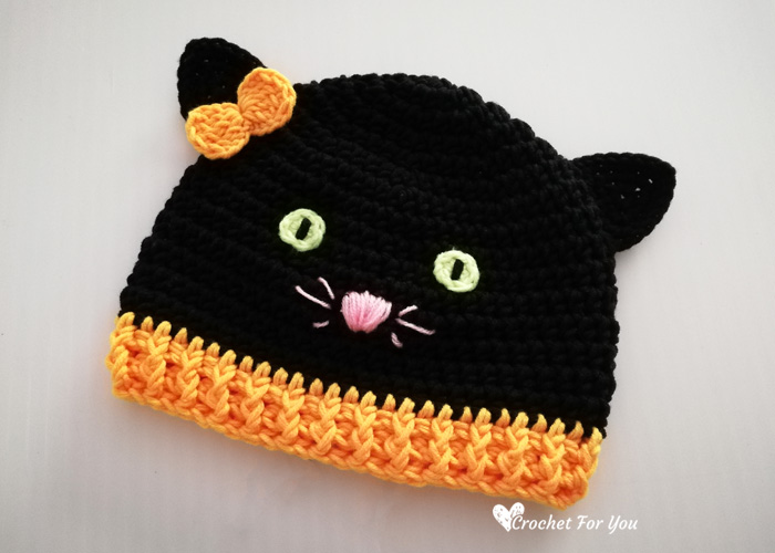 Black crochet cat hat with ears, yellow eyes, pink nose and an orange bow for toddlers