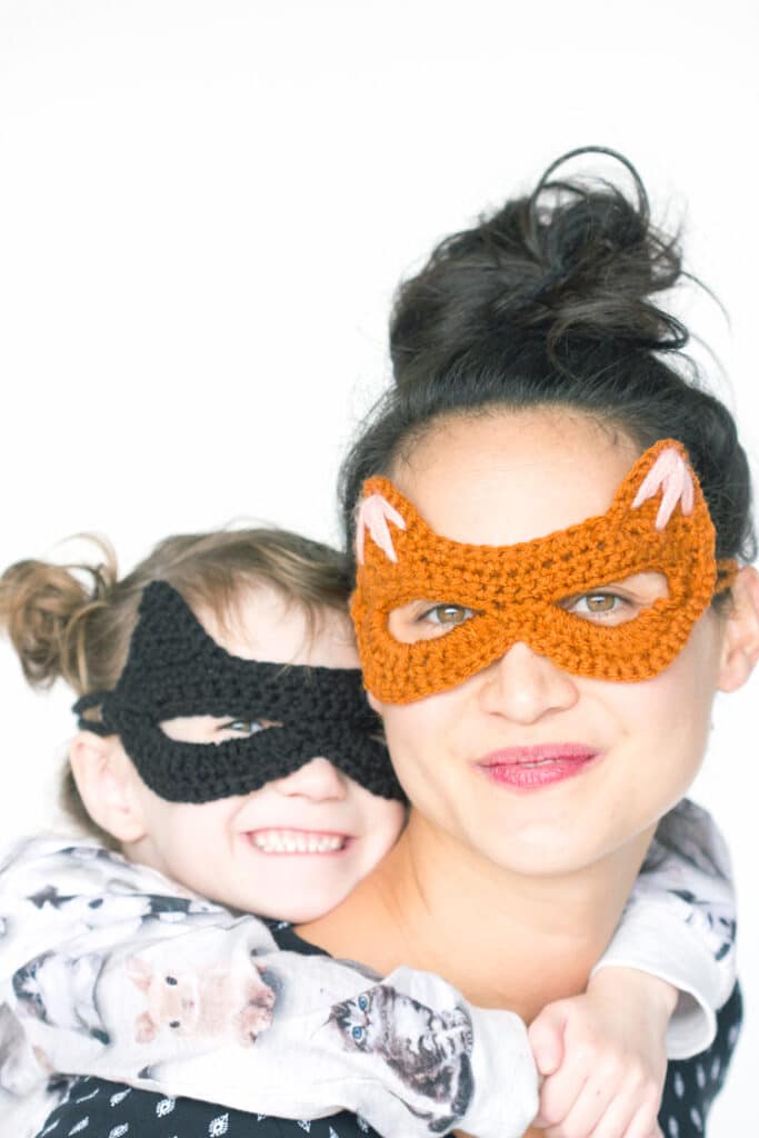 Woman in an orange crochet cat mask and a child in a black crochet mask