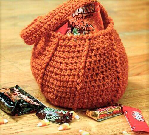 Orange crochet pumpkin trick-or-treat bag with raised ridges, filled with Halloween candy