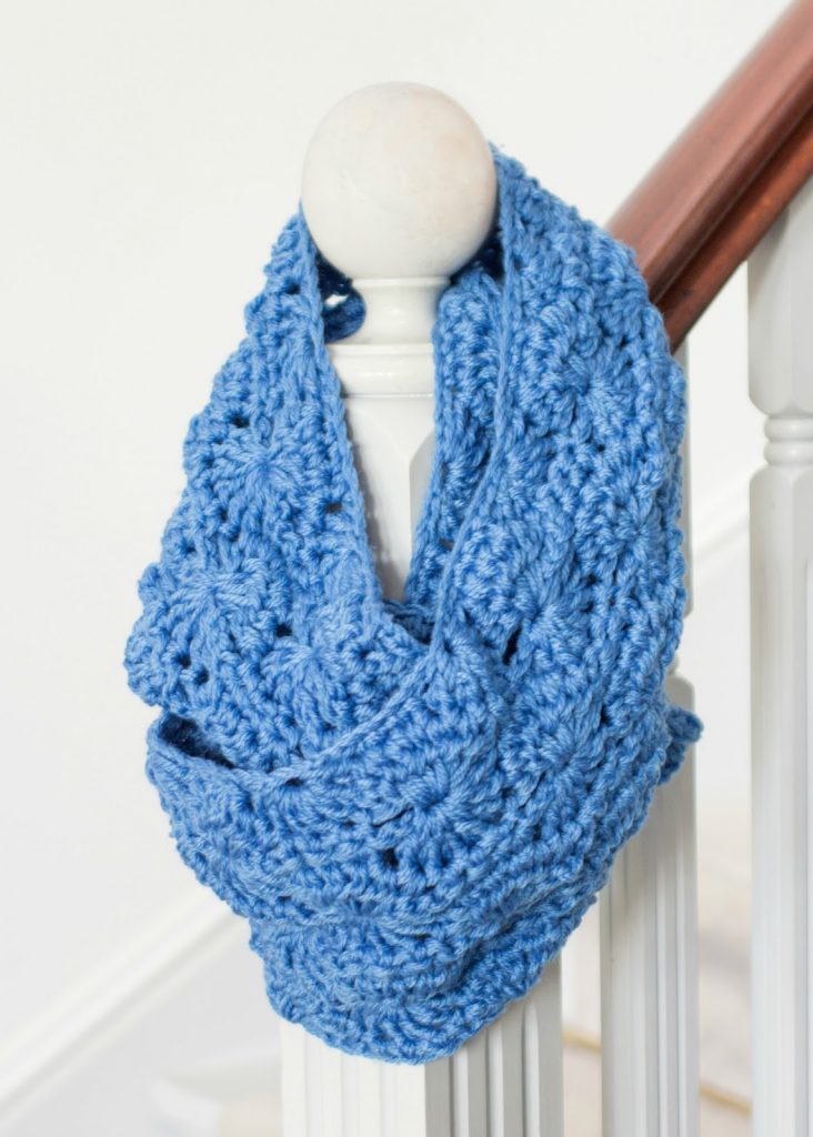 Chunky crochet infinity scarf in blue, hanging on a stair railing