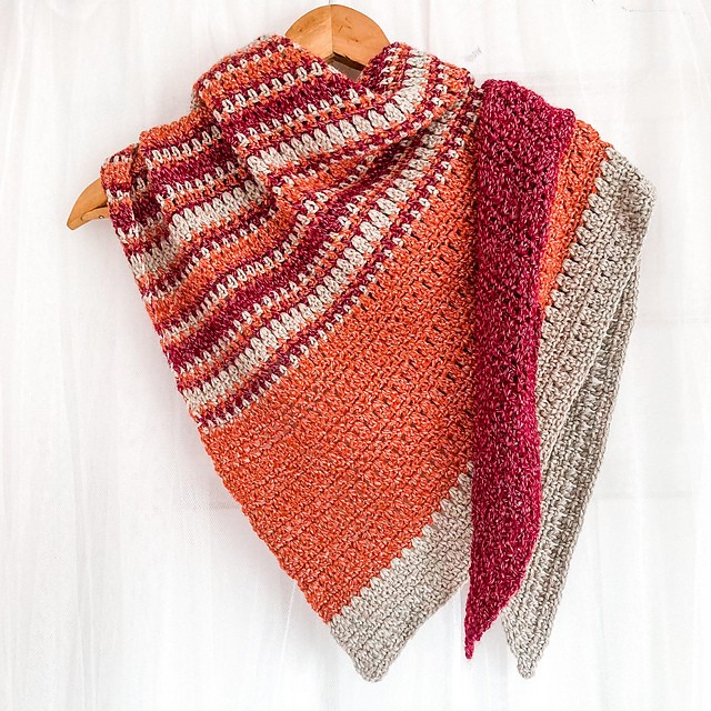 Autumn Meadow asymmetrical crochet shawl in orange, raspberry and beige stripes on a wooden hanger