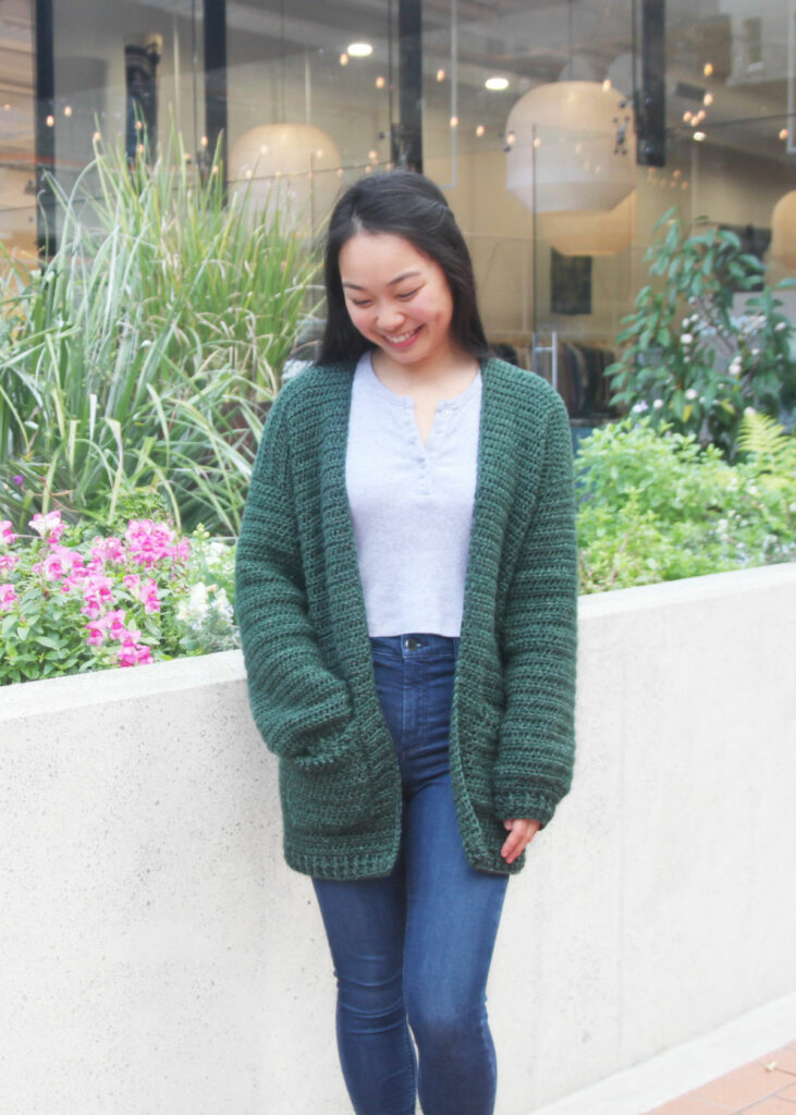 	Briar oversized crochet cardigan in forest green with two big pockets, worn with jeans