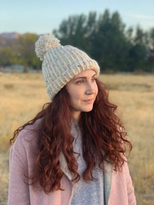 Woman in a field wearing a gray tweed crochet hat with a folded brim and pom pom