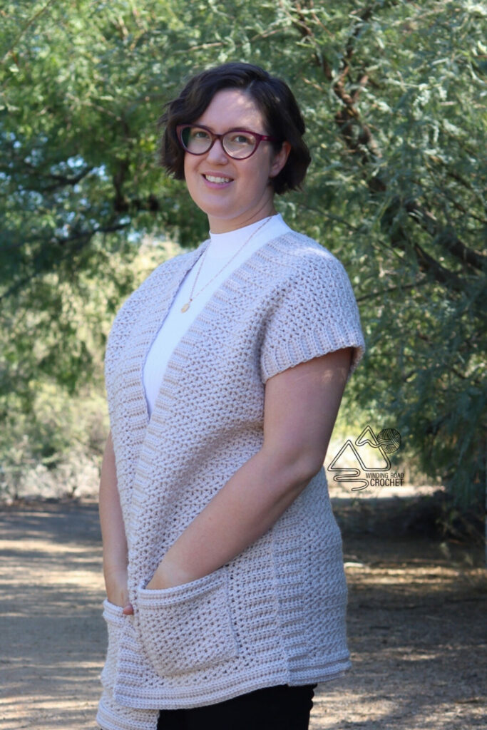 Short sleeve crochet cardigan in light lilac with front pockets, worn over a white turtleneck