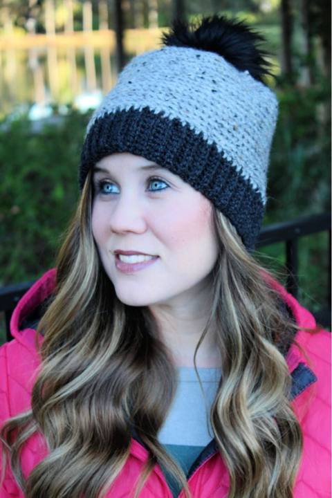 Woman wearing a gray camel stitch crochet beanie with a charcoal ribbed brim and black pom pom
