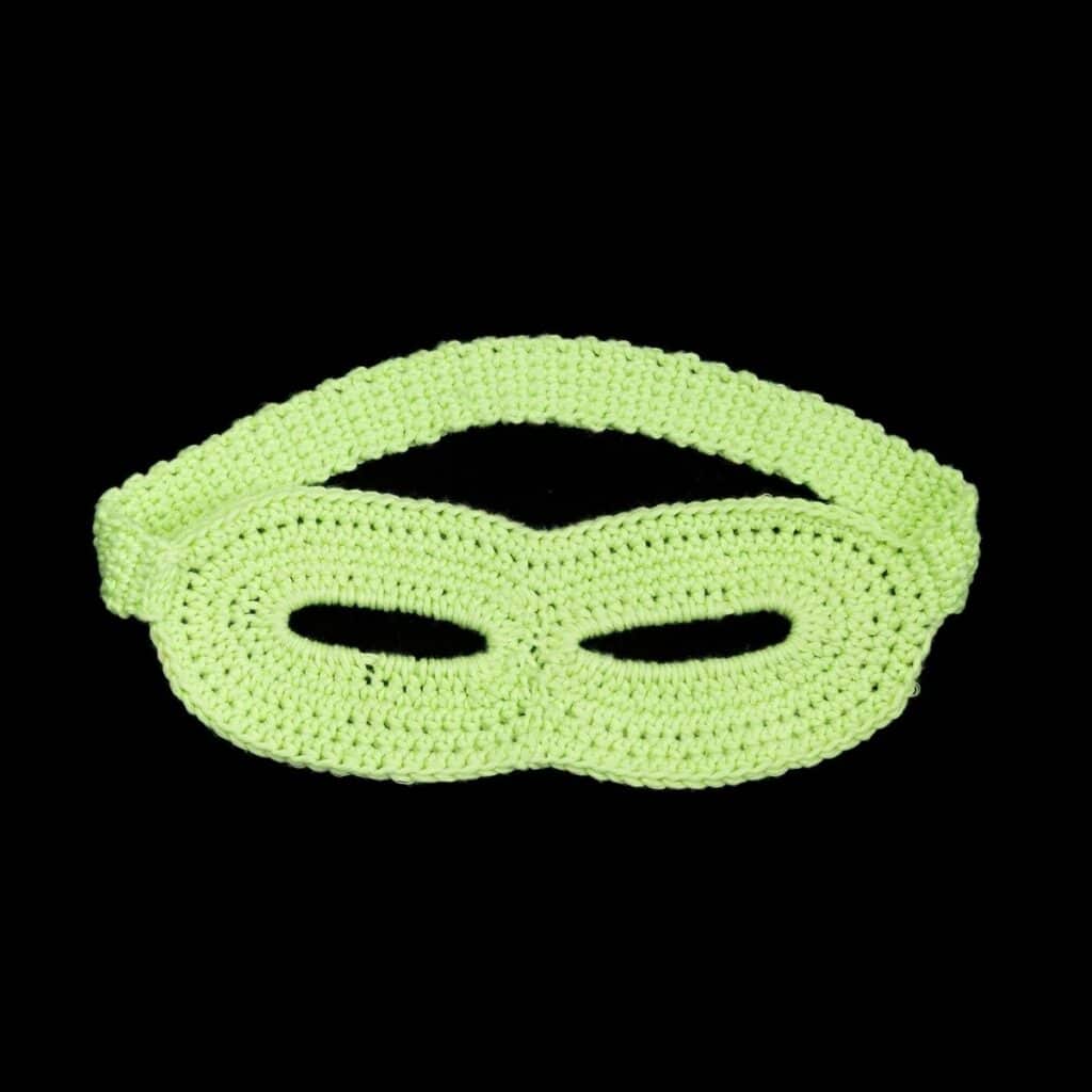 Glow-in-the-dark green crochet superhero mask on a black background
