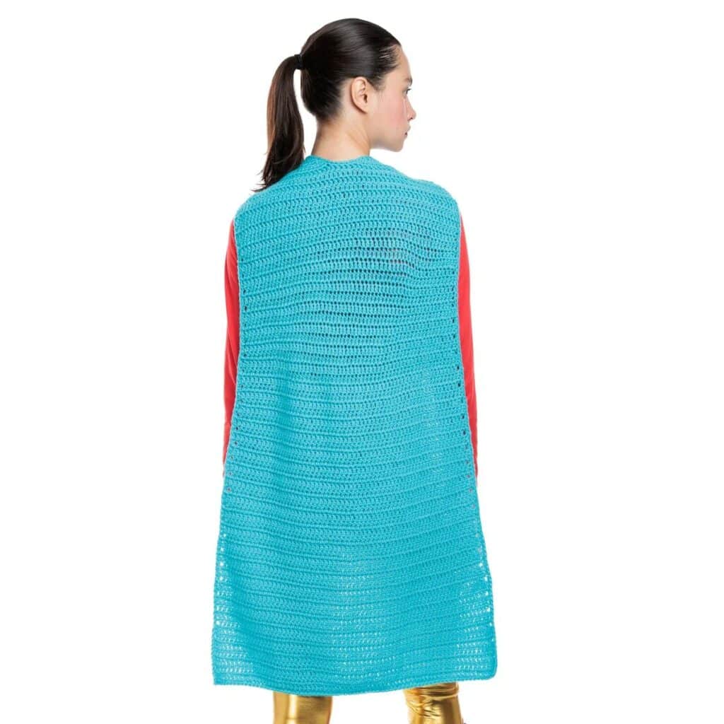 Back view of a long turquoise crochet superhero cape over a red top and gold leggings