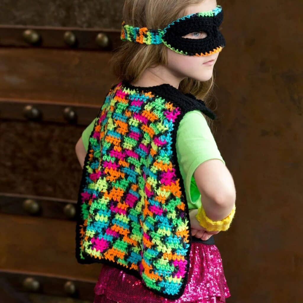 Girl in a neon crochet superhero cape, black mask with neon trim and yellow wrist cuff
