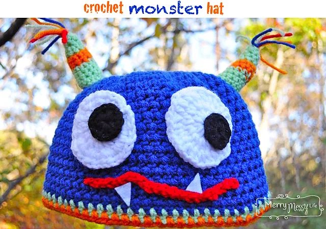 Blue crochet monster hat with big white eyes, a red mouth with fangs and striped horns